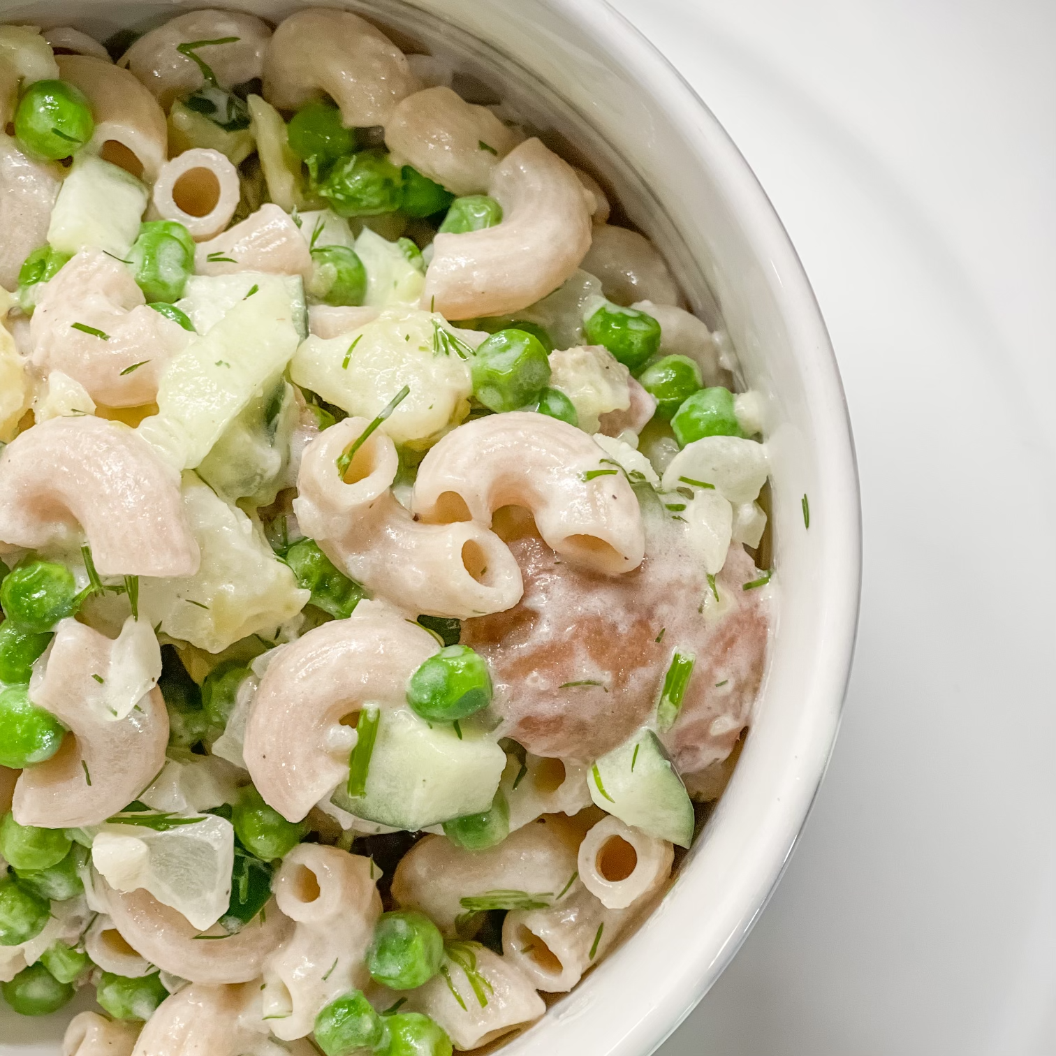 A delicious bowl of potato pasta salad with vibrant green peas and dill.